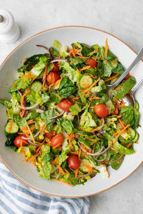 Fresh mixed salad with lettuce, cherry tomatoes, cucumbers, carrots, and red onion in a bowl. Healthy summer meal option.