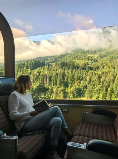 Woman reading a book on a train, enjoying scenic forest and mountain views through large window. Peaceful travel moment.