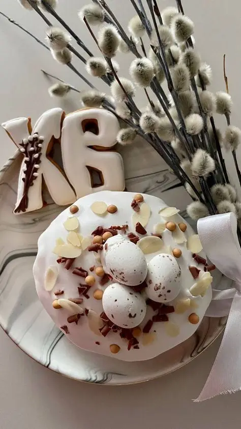 Elegant Easter cake with eggs and almonds, decorated with floral arrangement and chocolate letters on a marble-patterned plate.