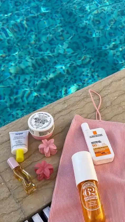 Skincare and sun care products by a poolside, including creams, sunscreen, and a pink striped bag. Perfect for a sunny day skincare routine.