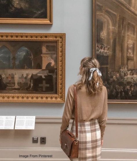 Woman with bow in hair admiring paintings in an art museum gallery.