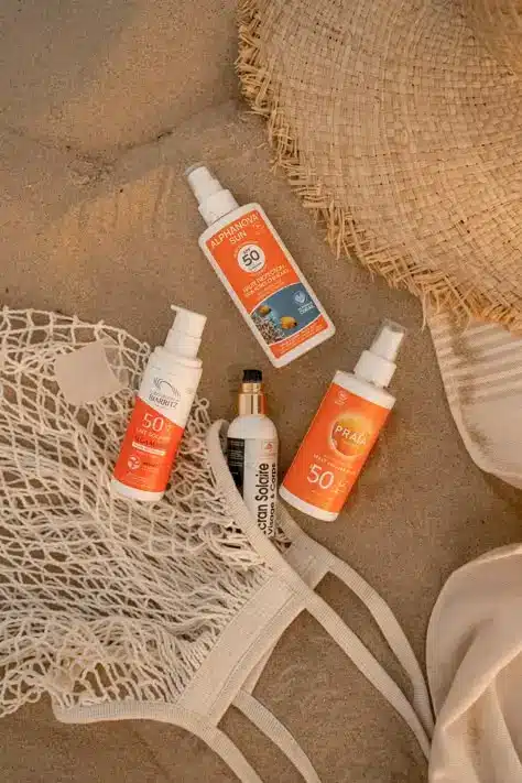 Sunscreen bottles on sandy beach with hat and bag, offering SPF 50 protection for sun safety and skincare.