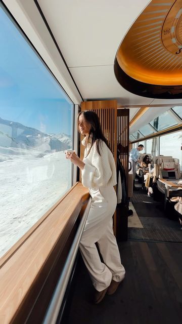 Person enjoying scenic snowy mountain view from a luxurious train with panoramic windows.