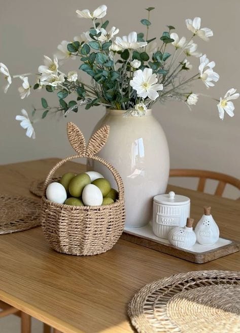 Woven basket with Easter eggs and a vase of white flowers on a wooden table, creating a rustic spring decor.