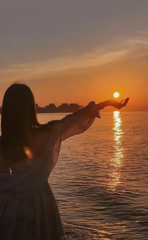 Silhouette of a woman holding the sun at sunset over the ocean, creating a serene and picturesque coastal view.