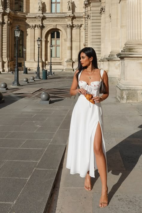 Woman in a white dress poses elegantly in front of a historic building, showcasing summer fashion.