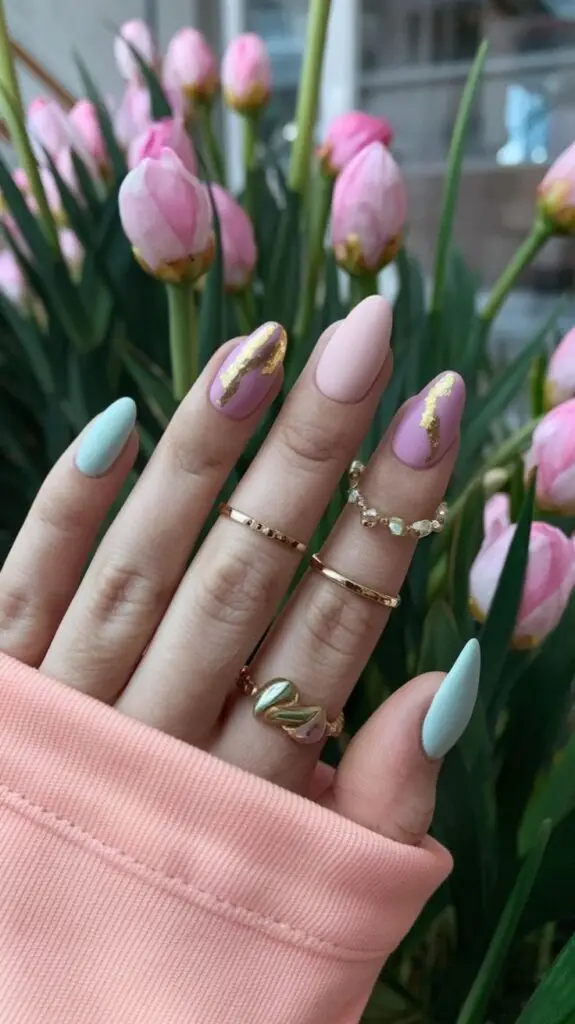 Stylish pastel nails with gold accents, surrounded by blooming pink tulips. Elegant rings add a touch of glamour.