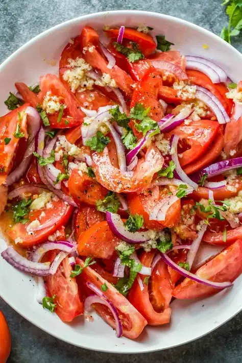 Fresh tomato salad with red onions, garlic, and herbs on a white plate; vibrant and healthy summer dish.