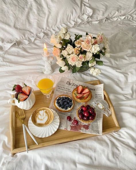 Elegant breakfast in bed setup: fruit tarts, cappuccino, orange juice, fresh roses. Relaxing morning vibe.