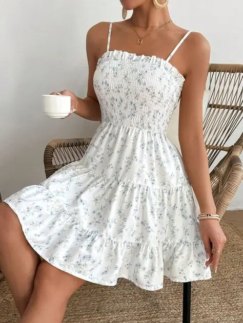 Woman in sleeveless floral dress holding a cup, sitting on a wicker chair, enjoying a relaxed moment indoors.
