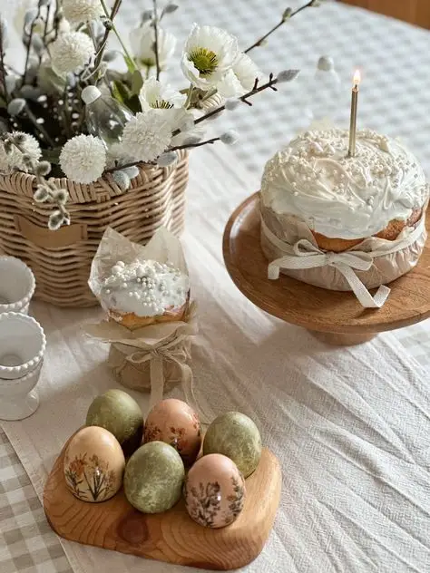 Easter celebration table with decorated eggs, floral centerpiece, and cake on a stand with a lit candle.