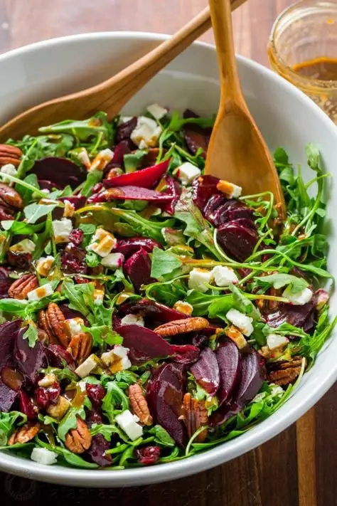 Fresh beet salad with arugula, feta, pecans, and vinaigrette in a white bowl. Healthy, colorful dish perfect for any meal.