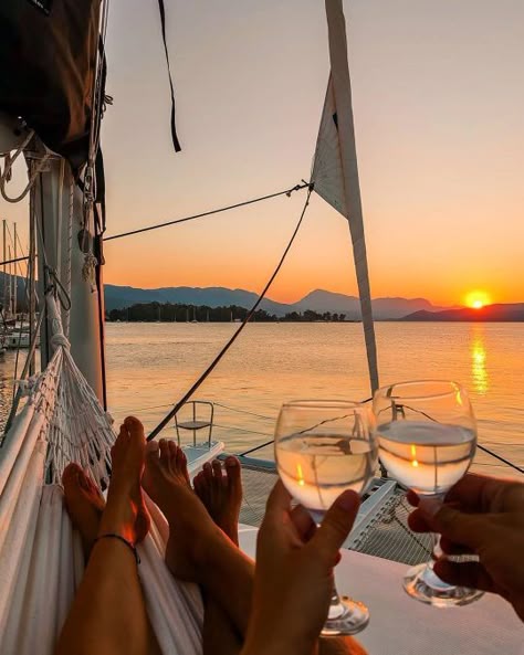 Couple on sailboat enjoying sunset, toasting with wine glasses, and relaxing in a hammock with serene sea and mountain view.