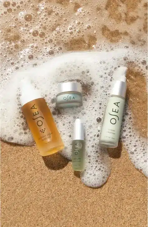 OSEA skincare products on sandy beach with ocean waves, showcasing natural beauty and marine-inspired wellness.