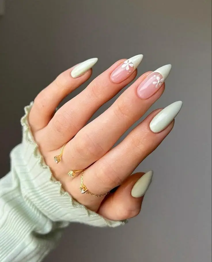 Stylish almond-shaped nails with white floral design, paired with gold rings and a cozy sleeve. Perfect for elegant nail art inspiration.