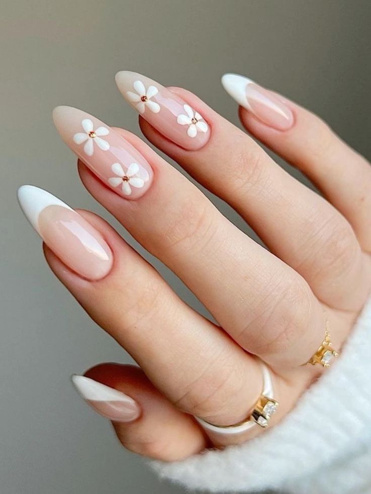Close-up of hand with elegant French manicure, featuring white daisy nail art on nude polish. Stylish and creative design.
