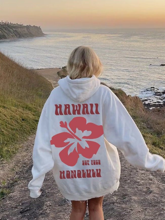 Person in a white Hawaii Honolulu hoodie walking along a scenic coastal path at sunset.