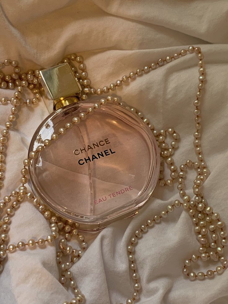 Chanel Chance Eau Tendre perfume on white fabric with pearl necklace, elegant and luxurious fragrance display.