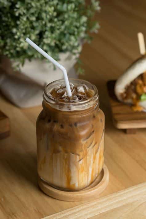 Iced coffee with caramel in a jar, accompanied by a bao bun on a wooden table. Fresh and delicious refreshment.