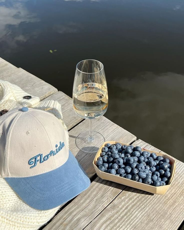 Blueberries, wine, and a Florida cap on a dock, reflecting a serene water view—a perfect setup for relaxation by the lake.