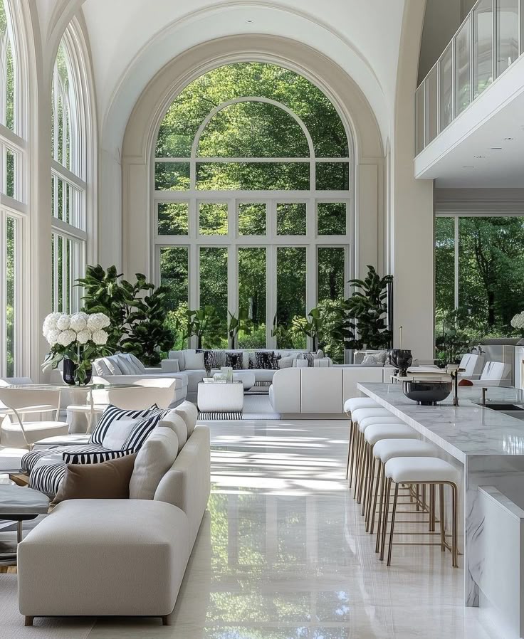 Luxurious modern living room with large arched windows, elegant white furniture, and lush greenery outside, creating a serene aesthetic.