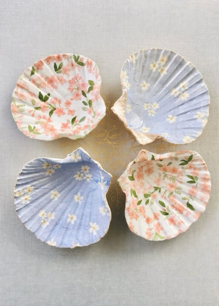 54e2445c-dd0d-4711-a74a-200b983f43e5 - Handy Home Decorative seashells with floral patterns on a textured background, featuring pink and blue designs with flowers.