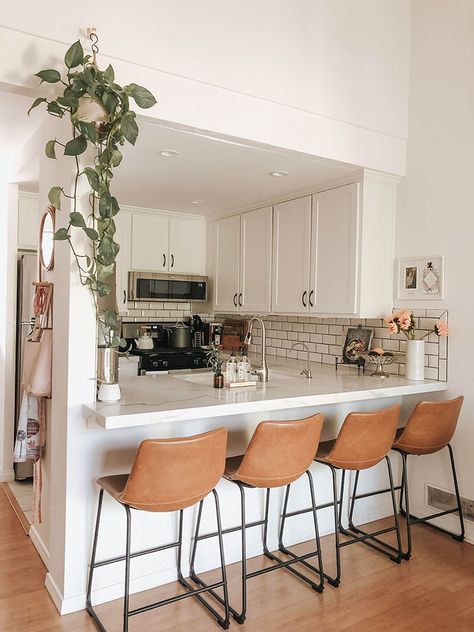 Modern kitchen with white cabinets, subway tile backsplash, barstools, and potted plant. Cozy and stylish interior design.