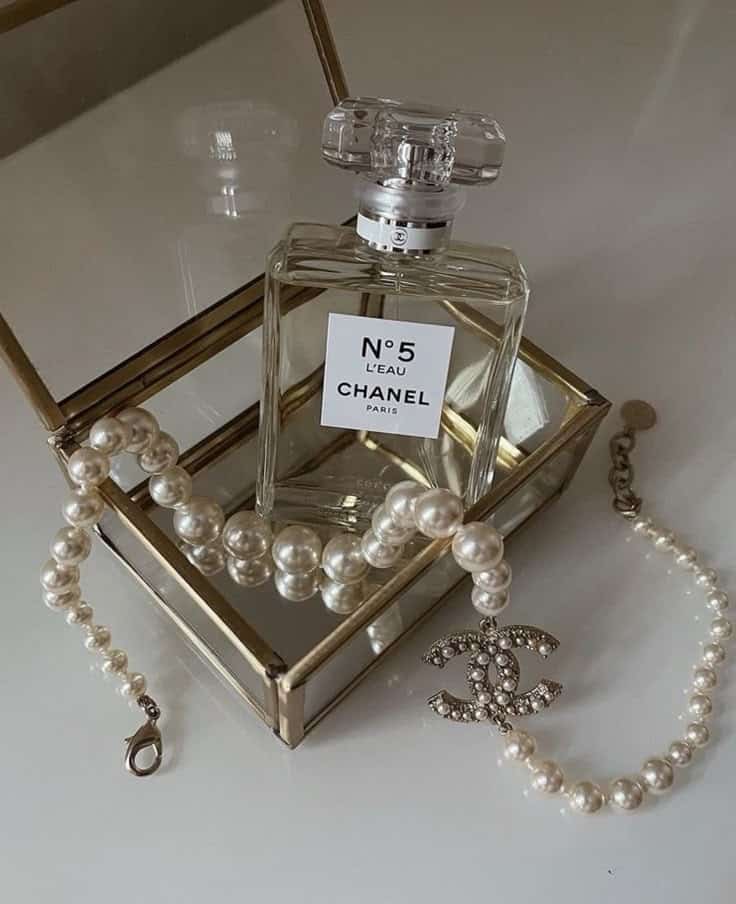 Chanel No. 5 perfume bottle in an elegant box with a pearl necklace adorned with a logo charm, showcasing luxury and elegance.