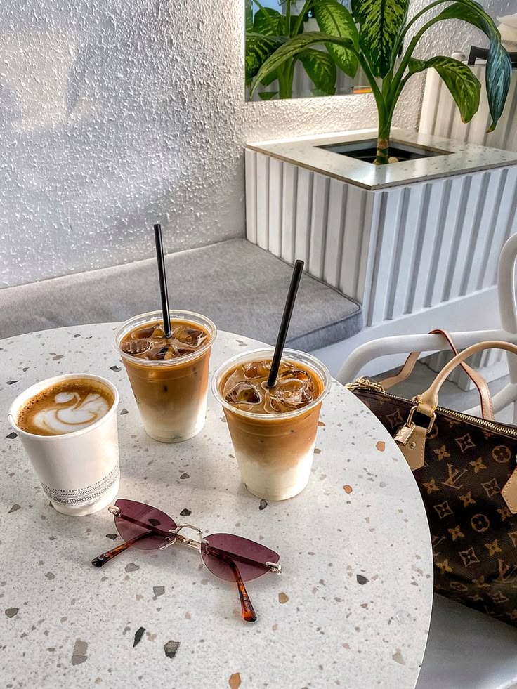 Iced and hot coffees on a terrazzo table with sunglasses and a stylish bag in a chic café setting.