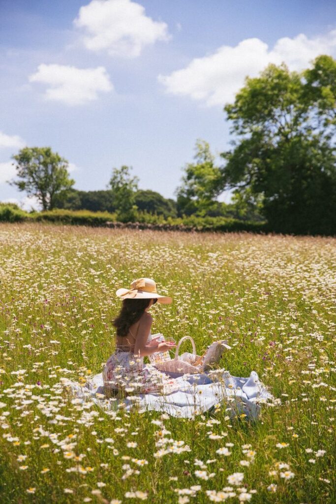 Woman enjoys a sunny picnic in a vibrant meadow of wildflowers, under a clear blue sky.