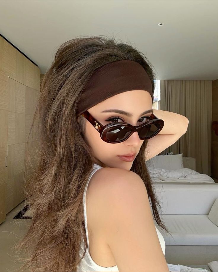 Woman with sunglasses and brown headband striking a pose indoors.