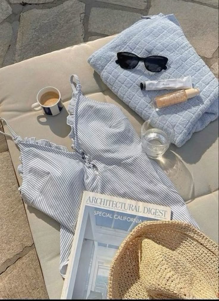 Sunny day essentials: striped top, coffee, magazine, towel, sunglasses, sunscreen, and a straw hat on a lounge chair.