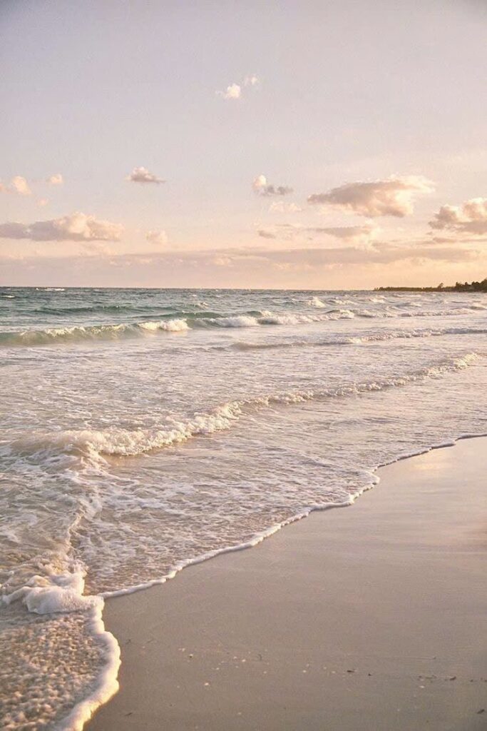 Serene beach at sunset with gentle waves and cloudy sky, creating a peaceful and calming seaside ambiance.