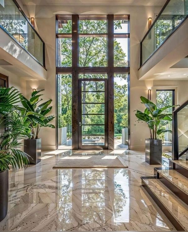 Luxurious modern foyer with high ceilings, marble floors, large windows, and lush indoor plants. Bright and elegant entryway design.