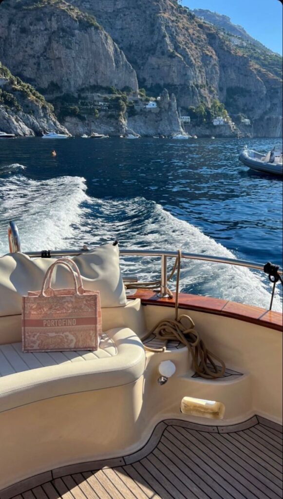 Luxurious boat ride along a scenic coastline, with a stylish Portofino bag on the seat, under sunny skies.
