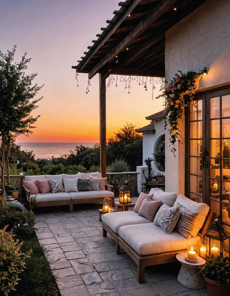 Cozy outdoor patio with seating, candles, and ocean view at sunset, under warm string lights for a perfect evening ambiance.