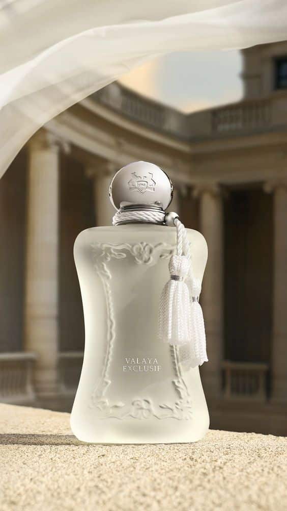 Elegant glass perfume bottle with white tassel, set against a classical architectural background, labeled Valaya Exclusif.
