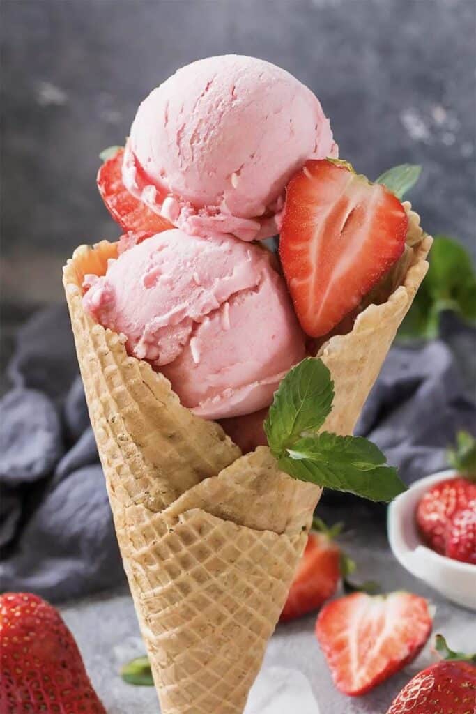 Strawberry Ice Cream - Handy Home Strawberry ice cream in a waffle cone garnished with fresh strawberries and mint leaves. Perfect treat for summer!