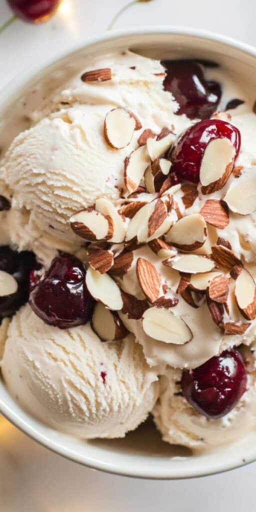 Creamy ice cream topped with toasted almonds and juicy cherries in a white bowl, perfect for a sweet treat or dessert delight.