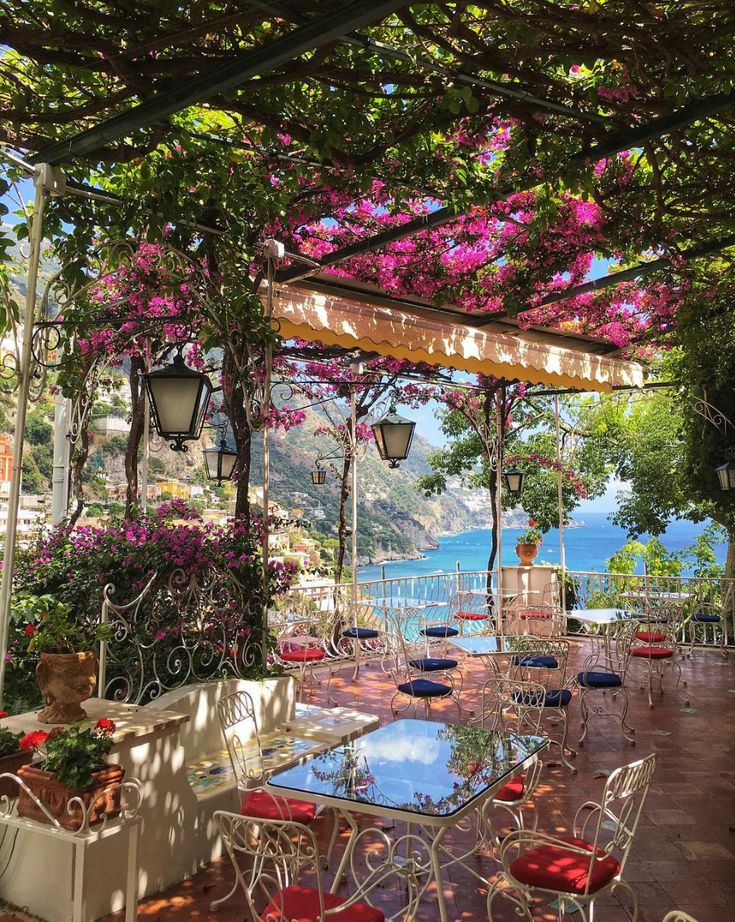 Scenic terrace with pink flowers and ocean view in Positano, Italy, featuring elegant wrought iron furniture and vibrant blooms.