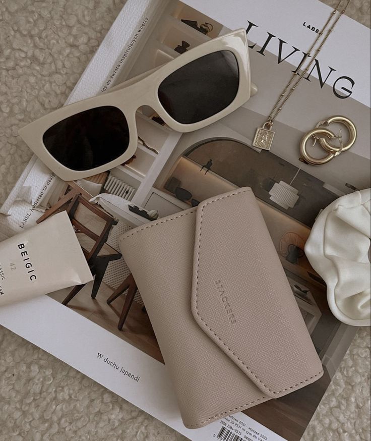 Chic flatlay with beige wallet, sunglasses, jewelry, cream, and a lifestyle magazine. Cozy and elegant aesthetic.