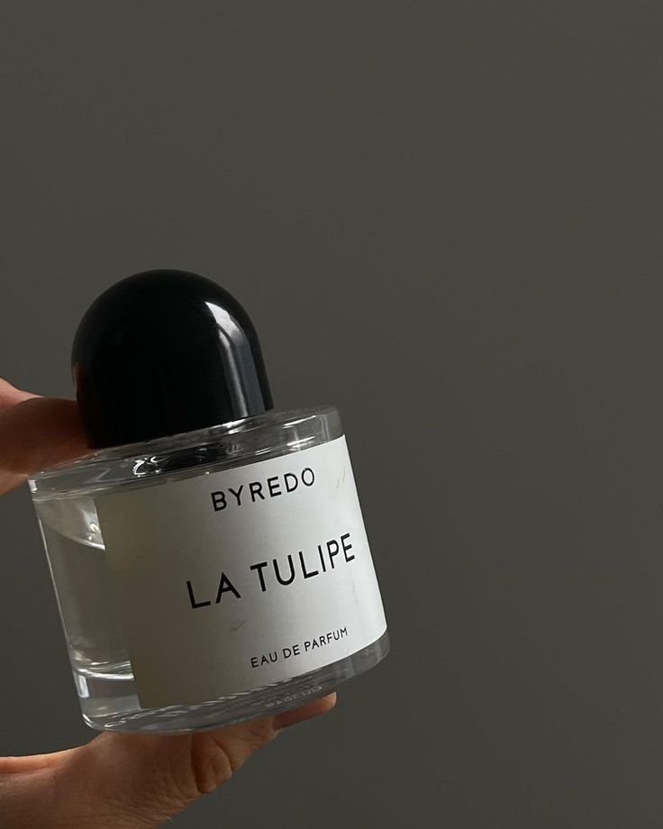 Clear perfume bottle labeled Byredo La Tulipe Eau de Parfum held against a dark background.
