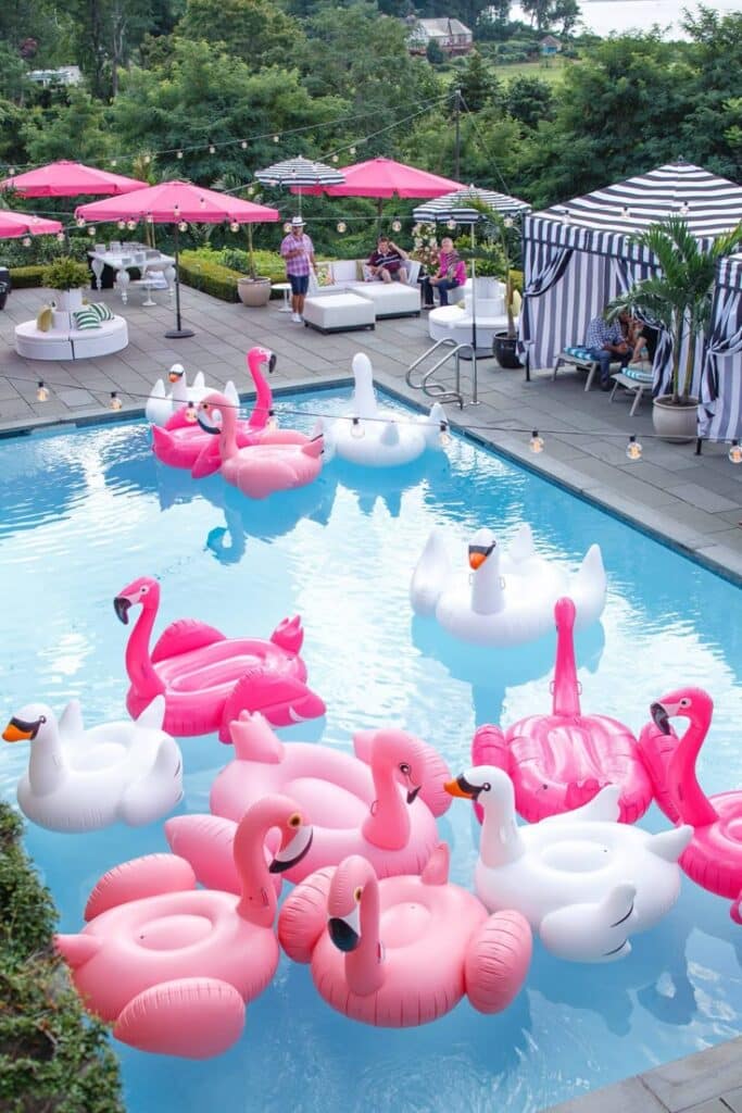 bcc3b698-f42d-49e4-bed3-2189736857b4 - Handy Home Pool party with pink flamingo and white swan floats, under pink umbrellas and striped canopies in a lush garden setting.