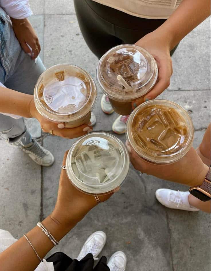 Four people holding iced coffee drinks in to-go cups, capturing a top view of a social gathering on a sidewalk.