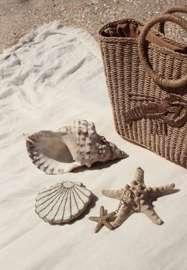 Beach-themed wicker bag with seashells and starfish decor on a sandy cloth background. Perfect summer vibes.