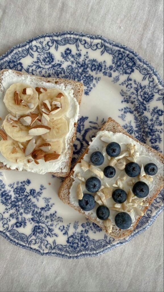 Delicious toast topped with banana, almonds, and blueberries on a vintage blue floral plate. Perfect breakfast idea.