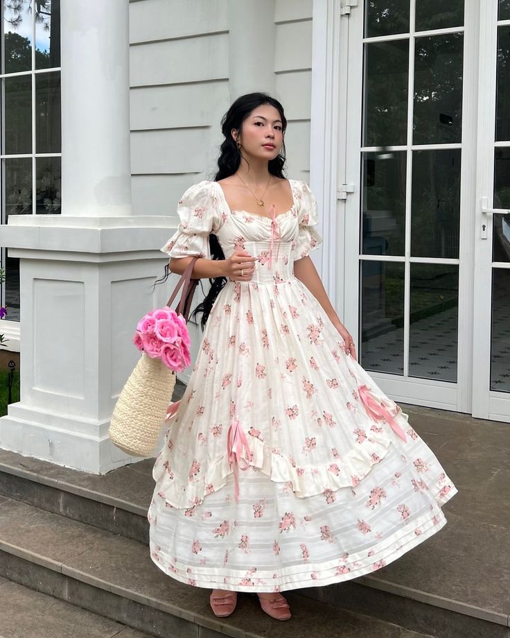 Woman in floral maxi dress with a straw bag, standing on steps in front of elegant building.
