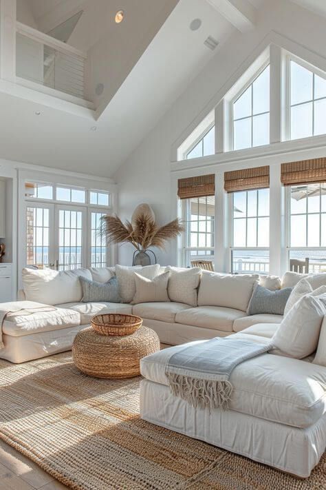 Bright and airy living room with large windows, white sectional sofa, woven rug, and coastal decor for modern beach house aesthetic.