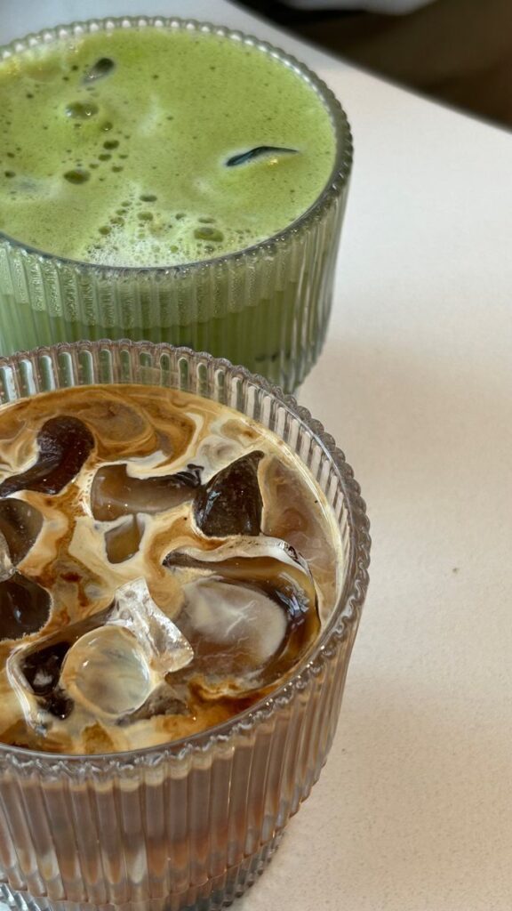 Iced matcha green tea and iced coffee with milk in ribbed glasses on a white table. Refreshing summer drinks.