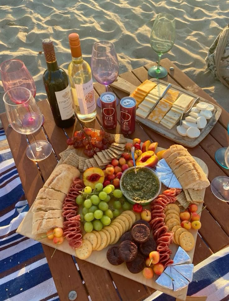 Beach picnic with wine, cheese, charcuterie board, and fruits on a wooden table, perfect for a sunset outing.